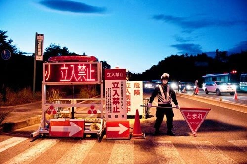 Police guards stand at a checkpoint at the entrance of the exclusion zone in Fukushima. In the evening, a red illuminated sign flashes the words: "No access... disaster law." Police guards stand at a checkpoint at the entrance of the exclusion zone in Fukushima. In the evening, a red illuminated sign flashes the words: "No access... disaster law."