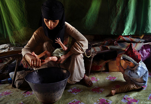 Child mothers: Asia, a 14-year-old mother, washes her new baby girl at home in Hajjah while her two-year-old daughter plays Child mothers: Asia, a 14-year-old mother, washes her new baby girl at home in Hajjah while her two-year-old daughter plays